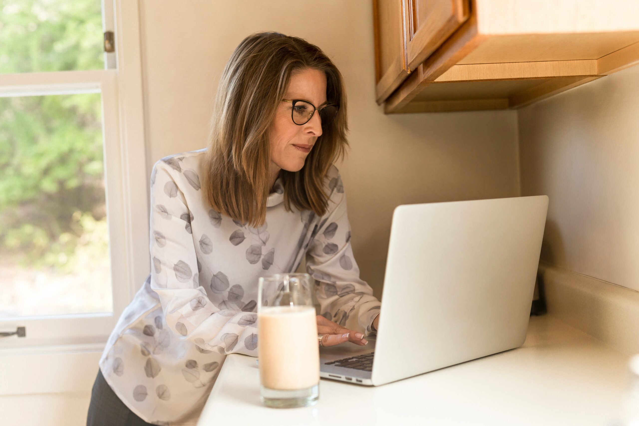 woman freelancer reviewing items on a laptop screen with a drink