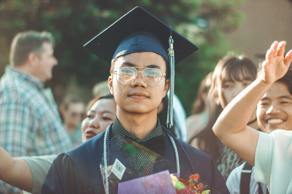 Asian male business degree graduate smiling during an outdoor graduation celebration with family and friends.