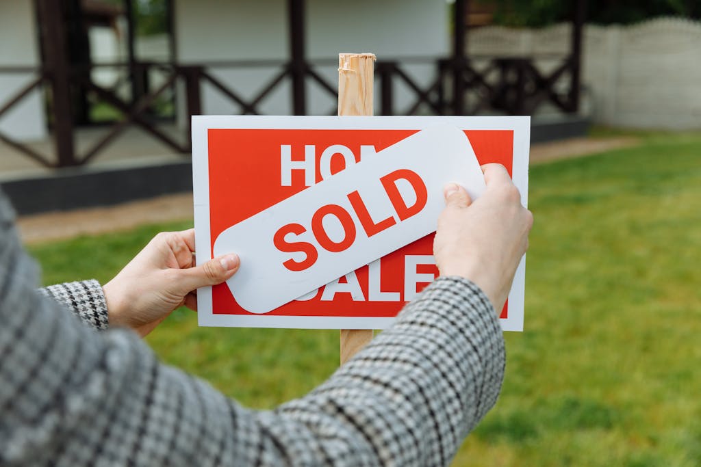 Close-up of hands placing a sold sticker on a real estate sign outside a house. Learn the answer to the question: should I sell my house?