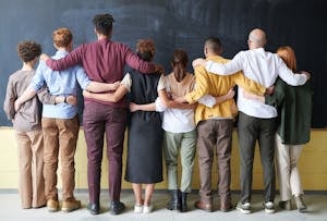 A diverse group of adults in casual outfits hugging in front of a chalkboard, symbolizing teamwork and community for solopreneurs